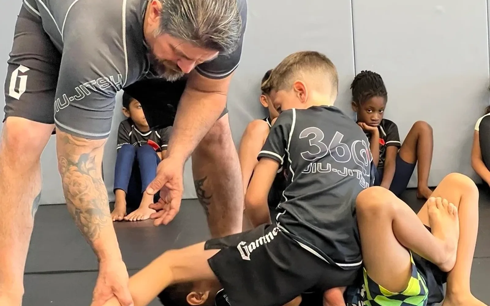 Coach guiding kids through technique on the mat